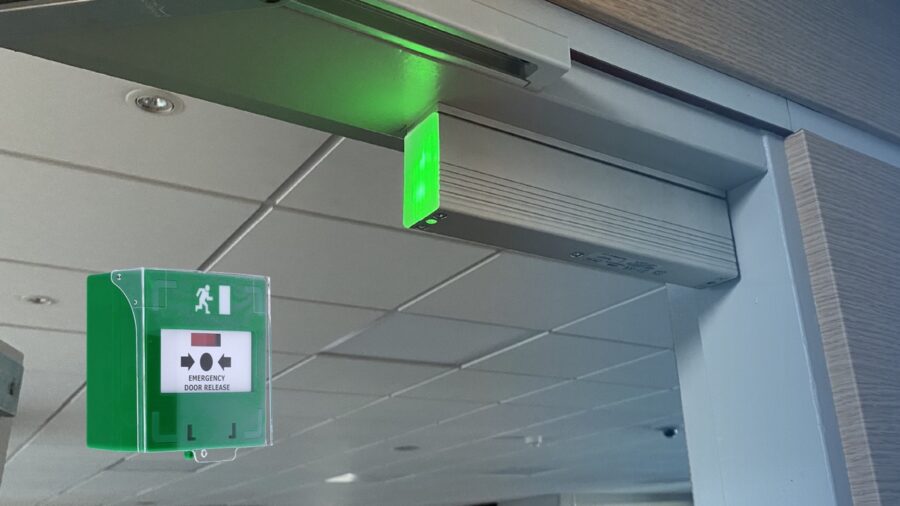 Nödlarmsknappen EM301 och ett elektromagnetiskt lås i ovankant på en glasdörr.
