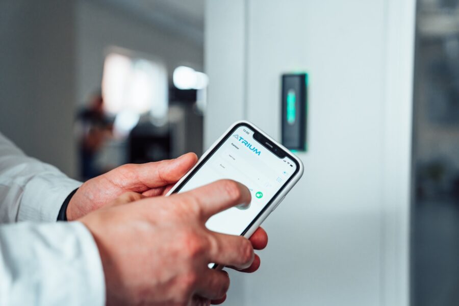 Man håller i en telefon för att öppna en dörr. på displayen ser man ett Atrium-system.